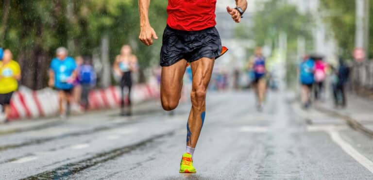 male runner leader running marathon city race, athlete run on wet asphalt after rain, muscular legs jogger